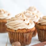 Close up shot of a Keto Spice Cake Cupcake on a white wooden table with a cinnamon stick in front.