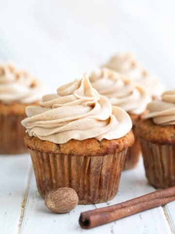 Close up shot of a Keto Spice Cake Cupcake on a white wooden table with a cinnamon stick in front.