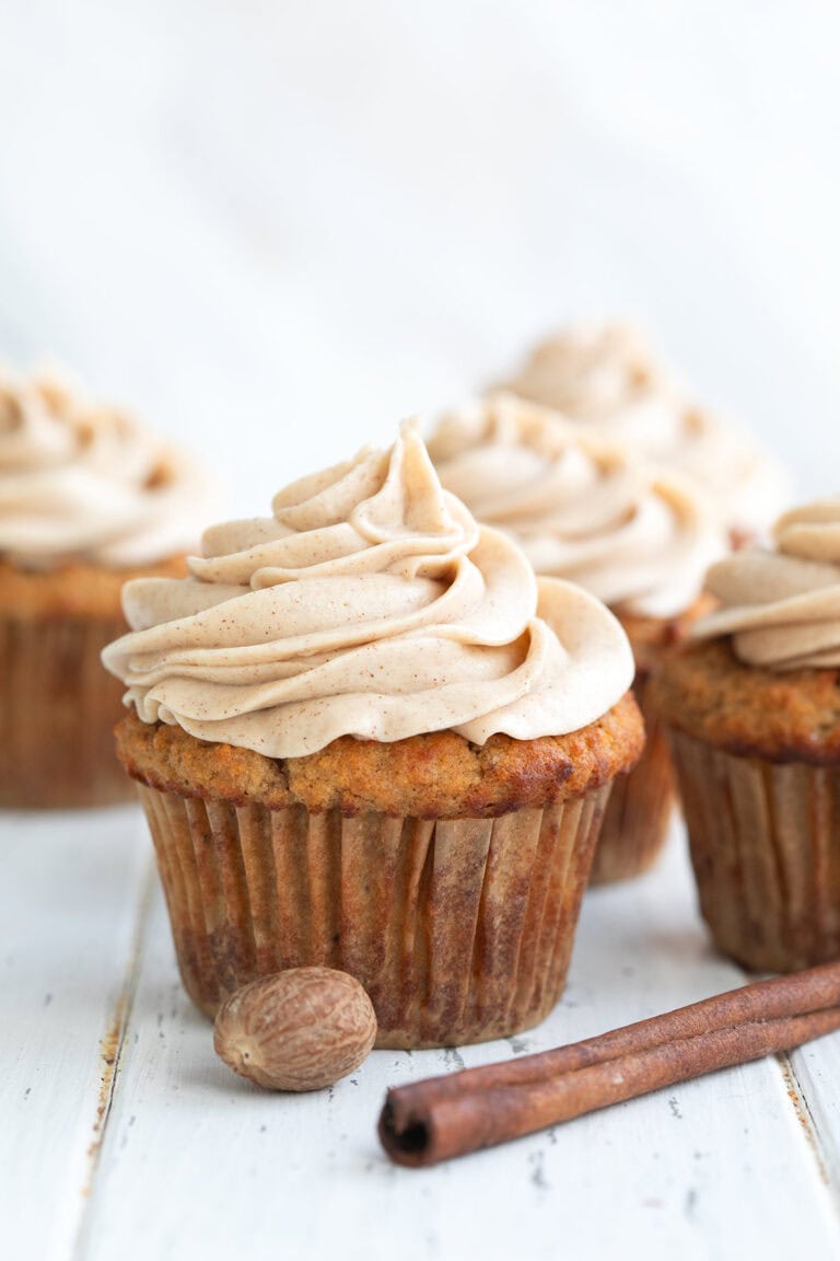 Close up shot of a Keto Spice Cake Cupcake on a white wooden table with a cinnamon stick in front.