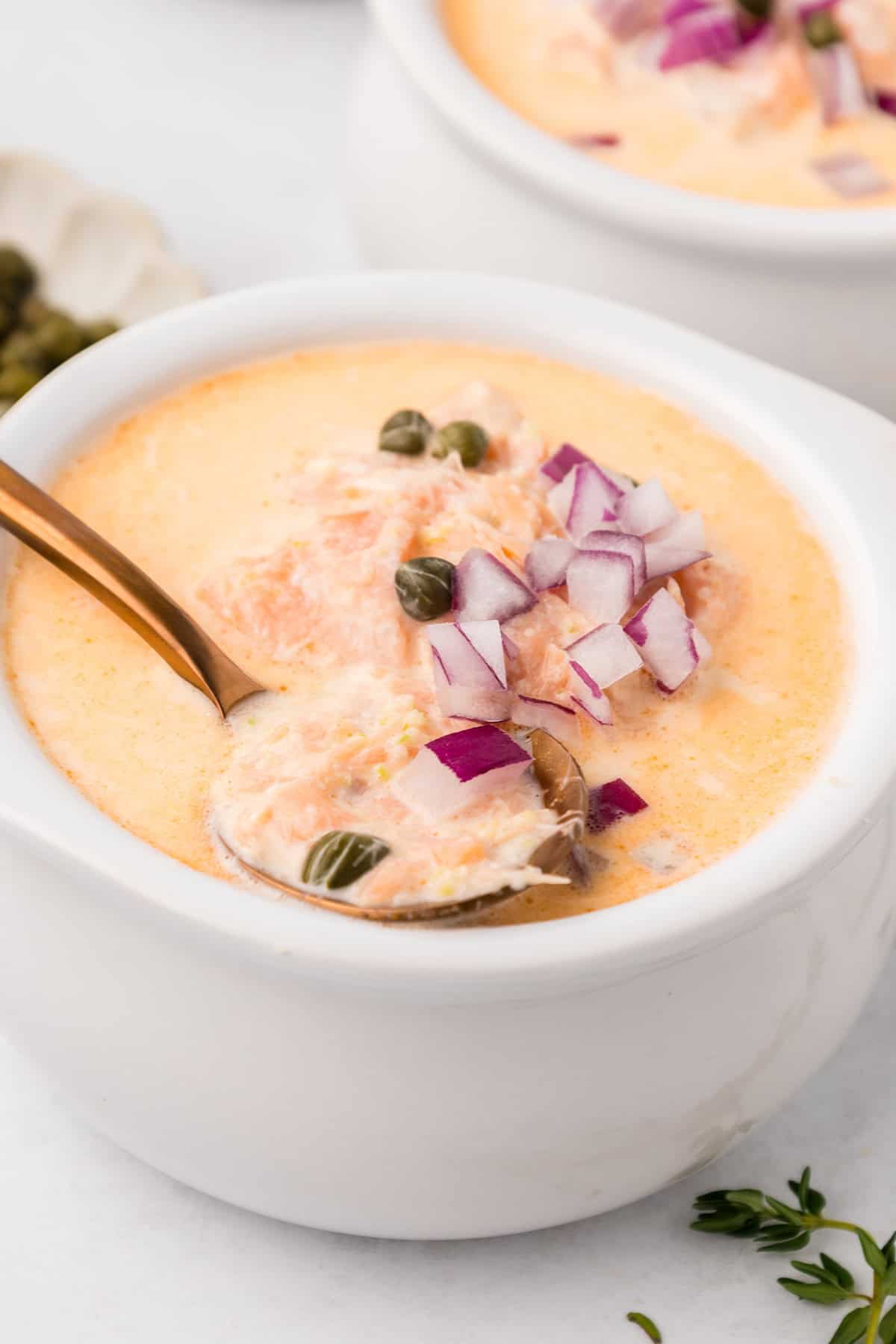 Close up shot of a white bowl filled with Smoked Salmon Chowder, with a spoon lifting some out.