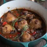 A teal dutch oven filled with Keto Coq au Vin on a dark wooden table.