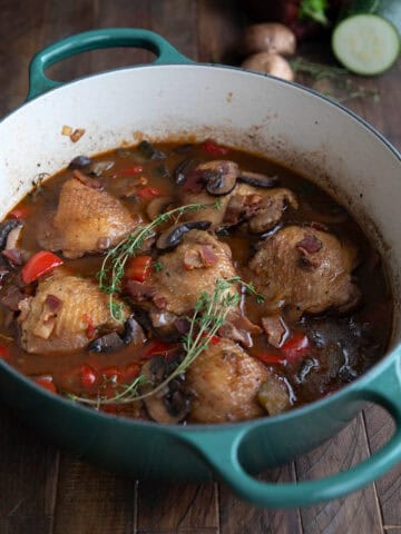 A teal dutch oven filled with Keto Coq au Vin on a dark wooden table.