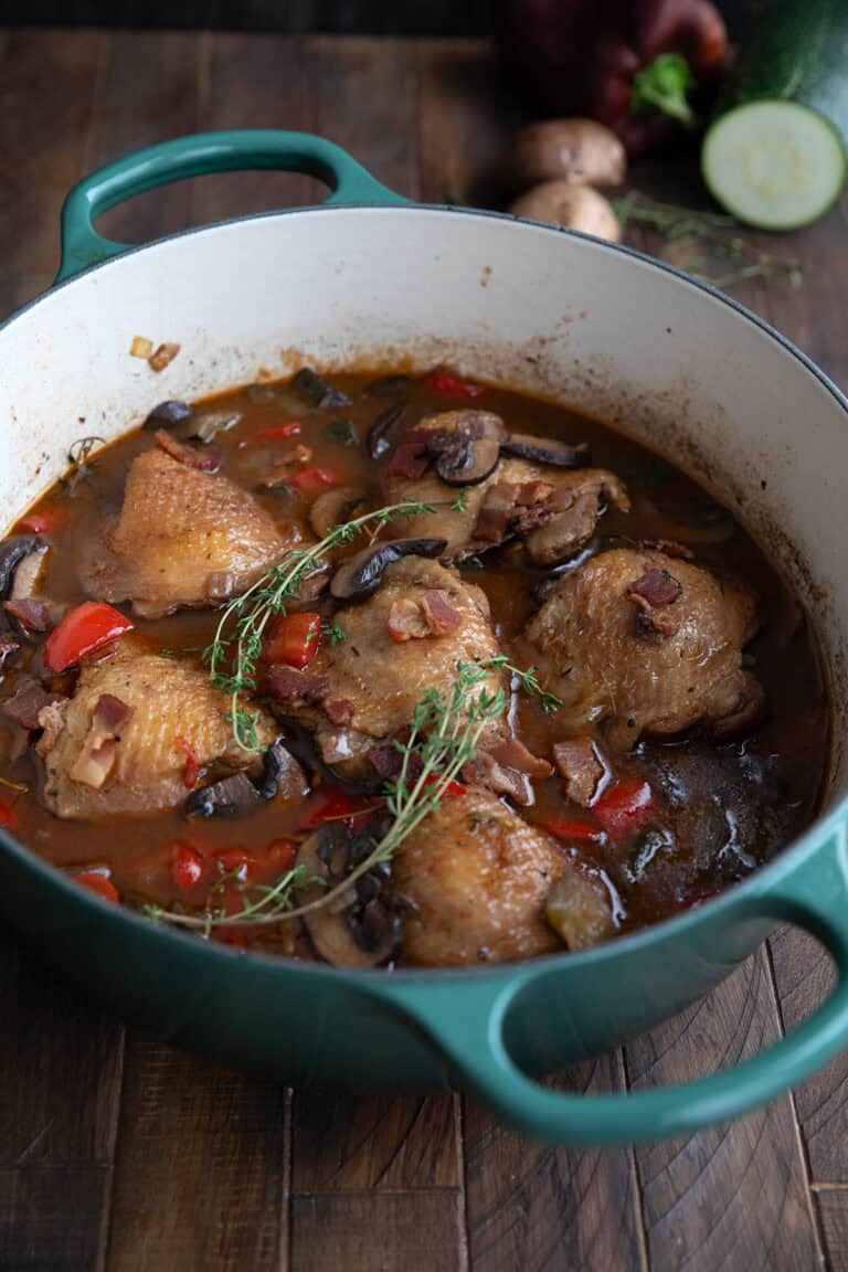 A teal dutch oven filled with Keto Coq au Vin on a dark wooden table.