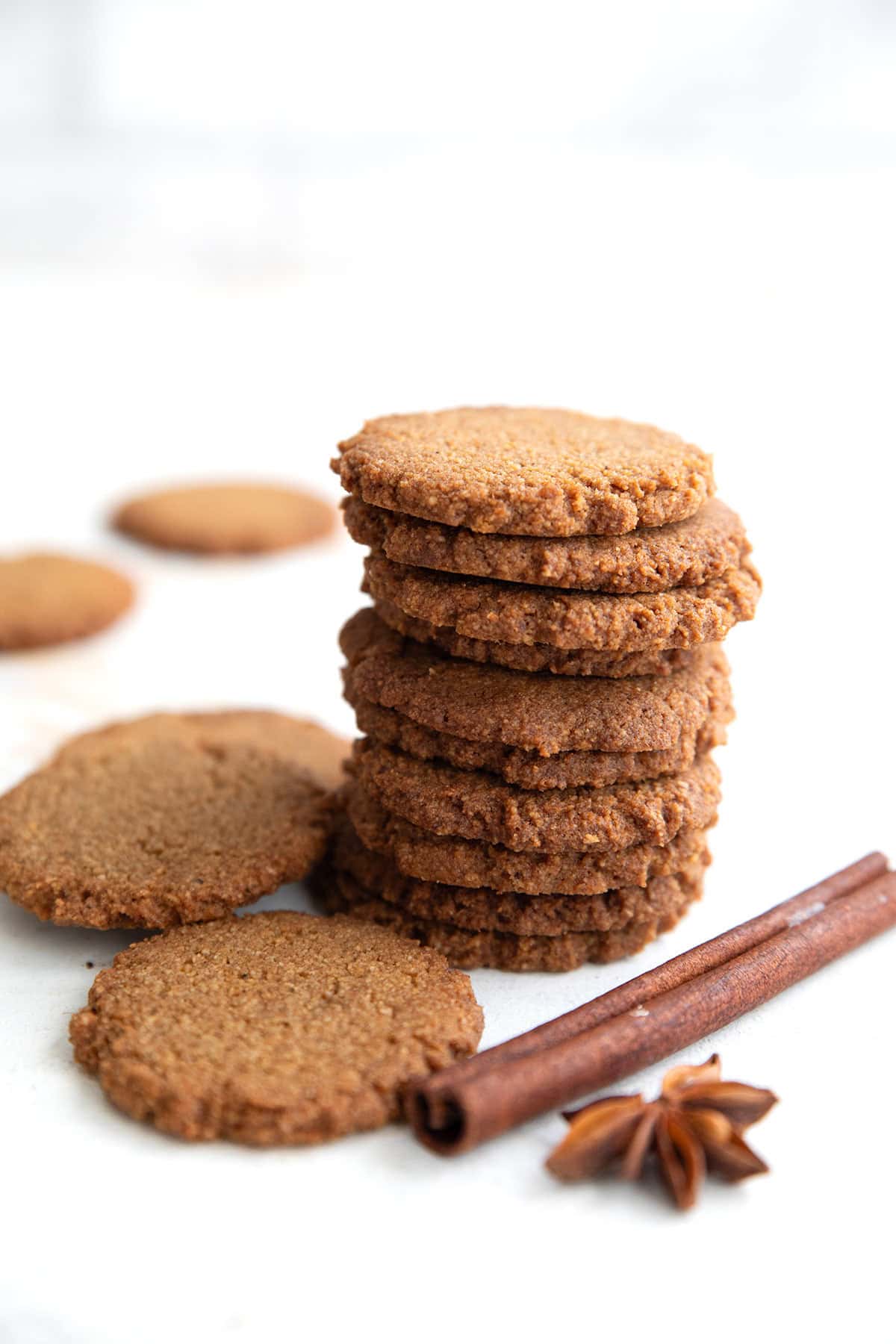 A stack of Keto Gingersnap Cookies on a white table with cinnamon and star anise.