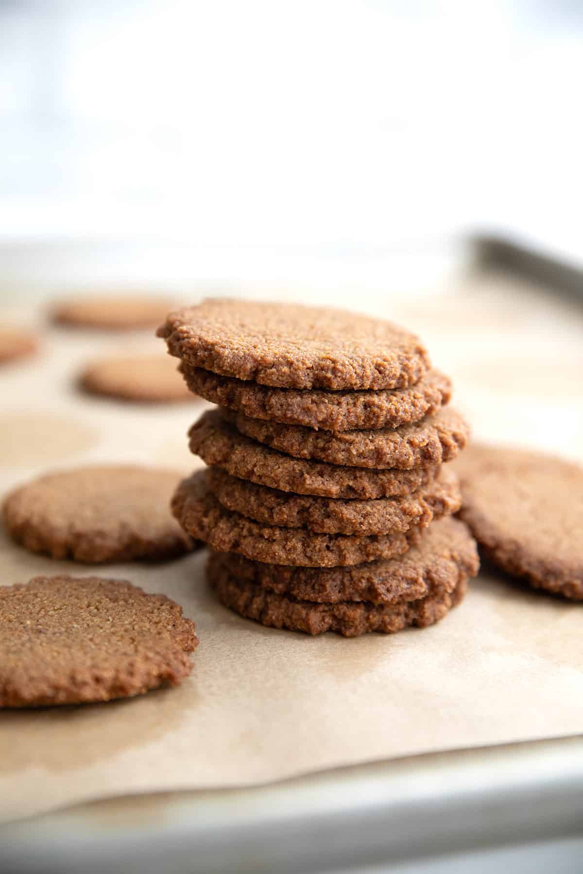 A stack of freshly baked Keto Gingersnap Cookies on a parchment lined cookie tray.