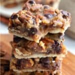 Titled image of a stack of Keto Pecan Pie Bars on a wooden cutting board with a bite taken out of the top bar.