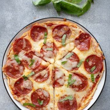 Top down image of cottage cheese protein pizza on a white plate with a sprig of fresh basil.