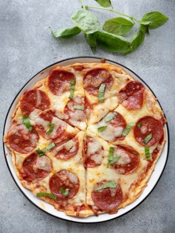 Top down image of cottage cheese protein pizza on a white plate with a sprig of fresh basil.