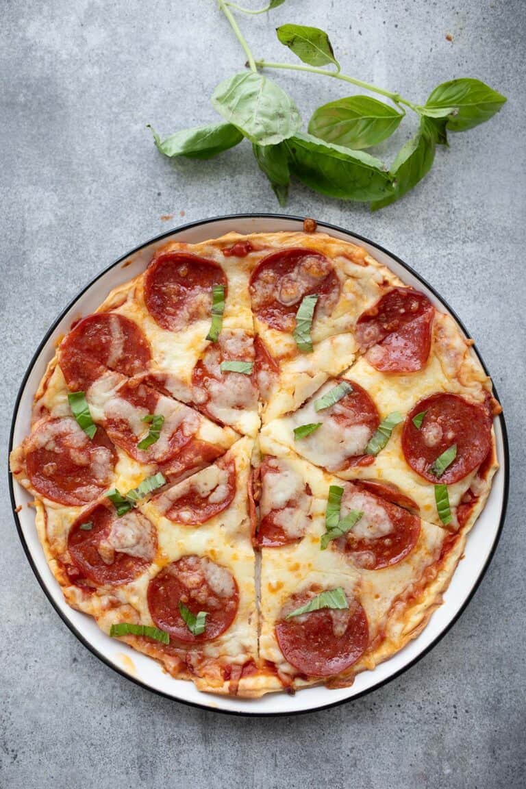 Top down image of cottage cheese protein pizza on a white plate with a sprig of fresh basil.