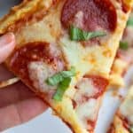 Titled Pinterest image of a hand holding up a slice of keto protein pizza.