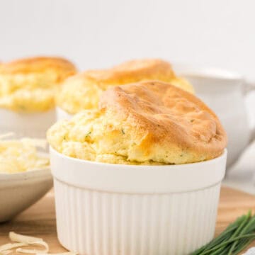 A Keto Cheese Soufflé in a white ramekin on a wooden cutting board, with chives.