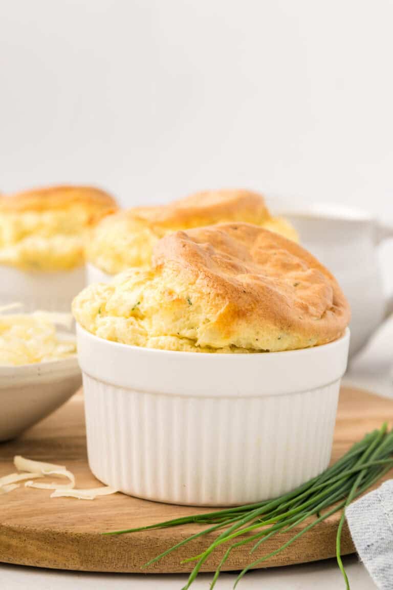 A Keto Cheese Soufflé in a white ramekin on a wooden cutting board, with chives.