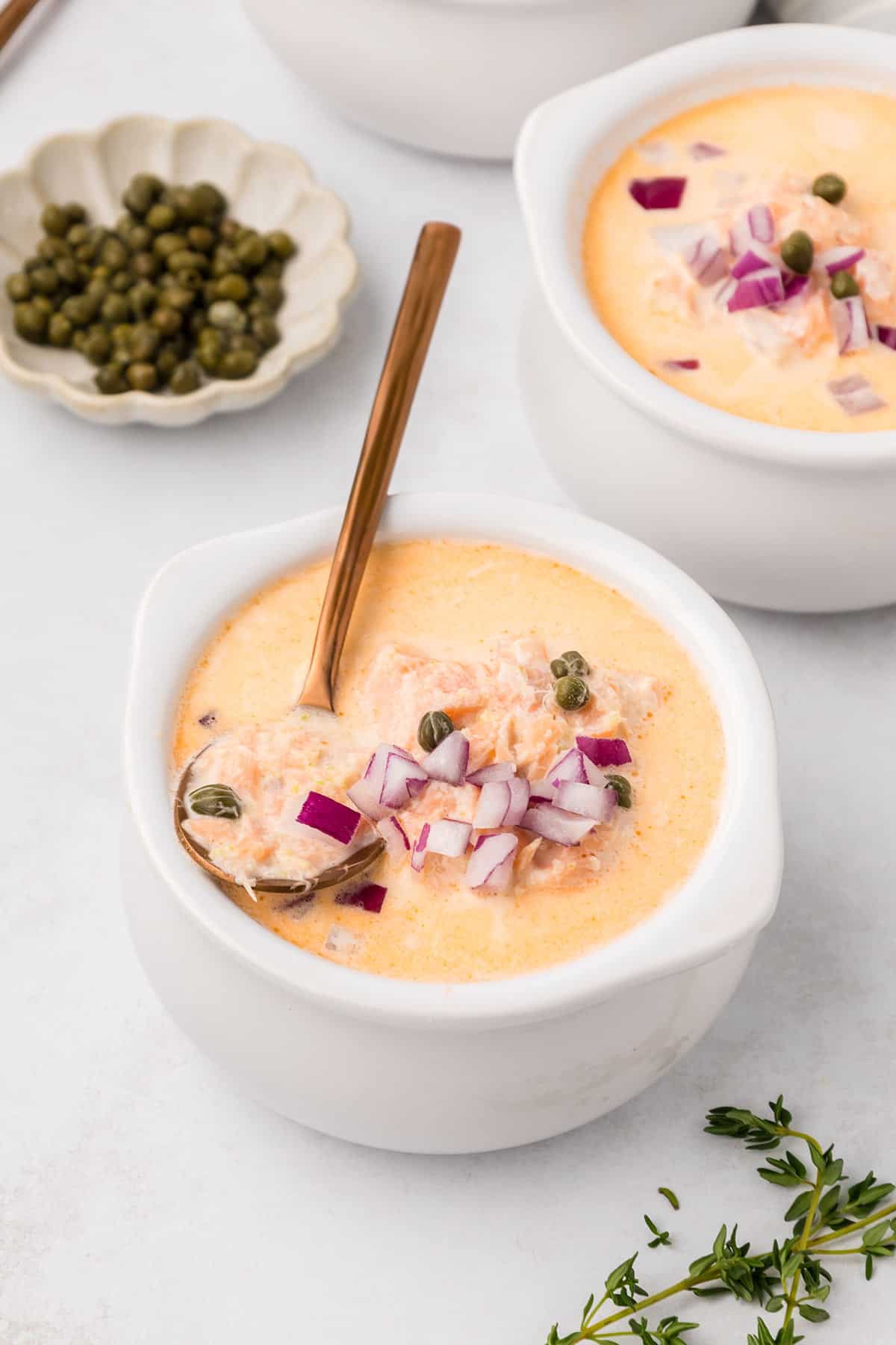 A white bowl filled with Keto Smoked Salmon Chowder with a copper colored spoon in it.