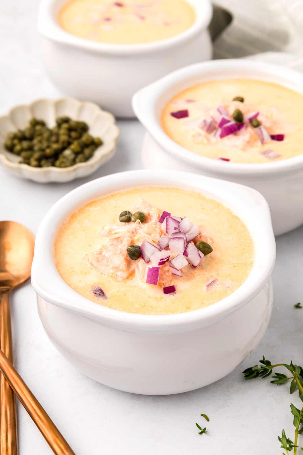 Three white bowls filled with Smoked Salmon Chowder on a light gray tabletop.