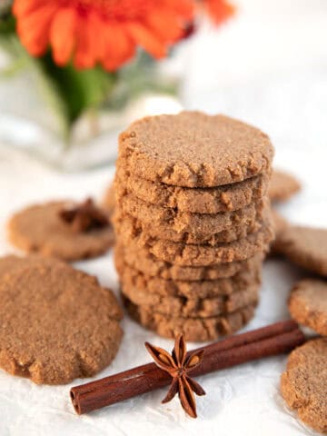 A stack of Keto Gingersnap Cookies with cinnamon and star anise, and orange Gerbera daisies in the background.