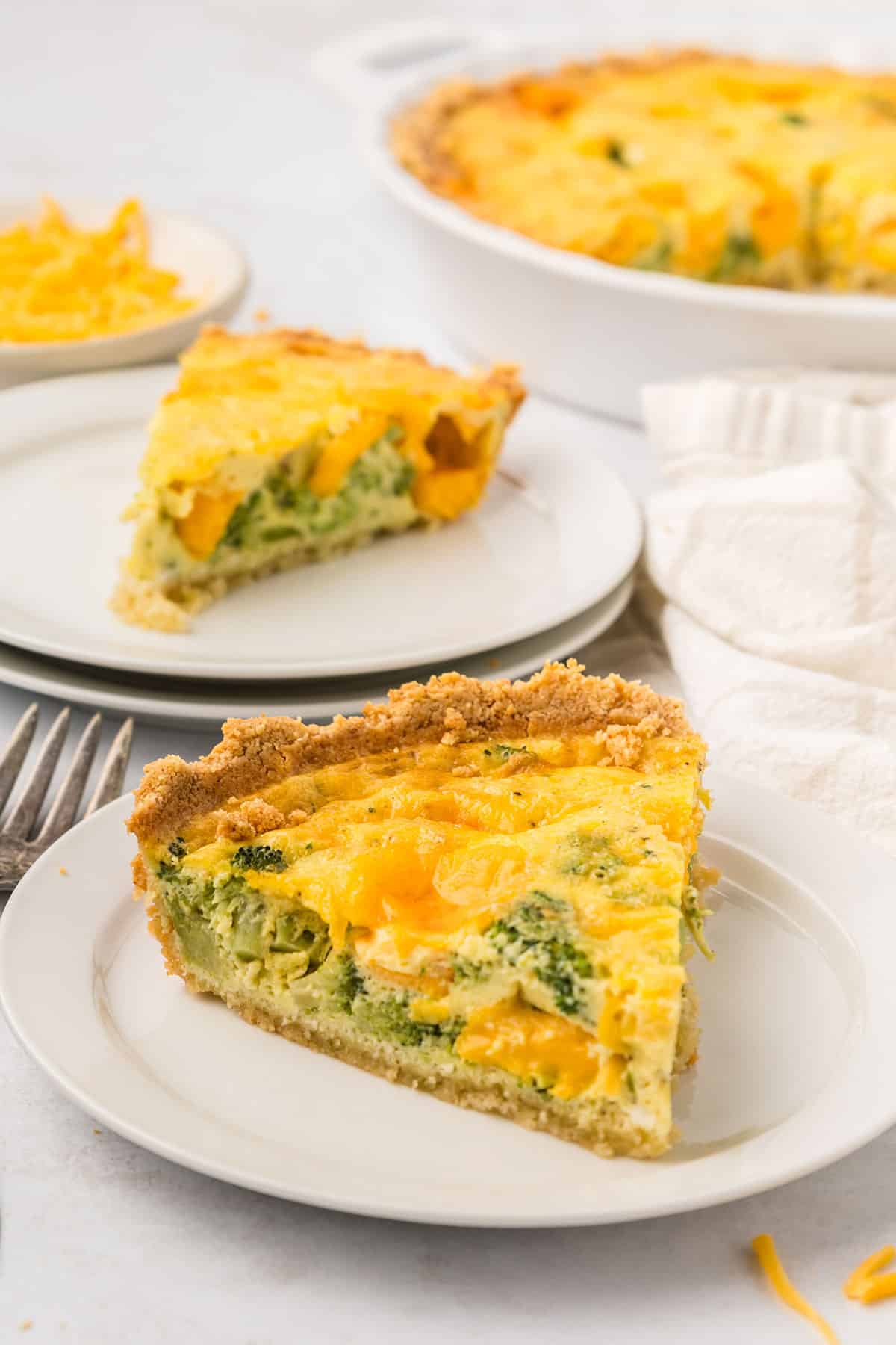 A slice of Keto Broccoli Cheese Quiche on a white plate with another slice in the background.