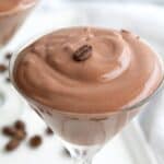 Titled image of keto chocolate protein mousse in a glass dessert dish with a coffee bean on top.