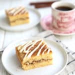 Two slices of Keto Cinnamon Roll Coffee Cake on white plates with a cup of coffee in an antique red patterned cup.