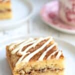 Titled image of a slice of Keto Cinnamon Roll Coffee Cake on a white plate on a white wooden table.