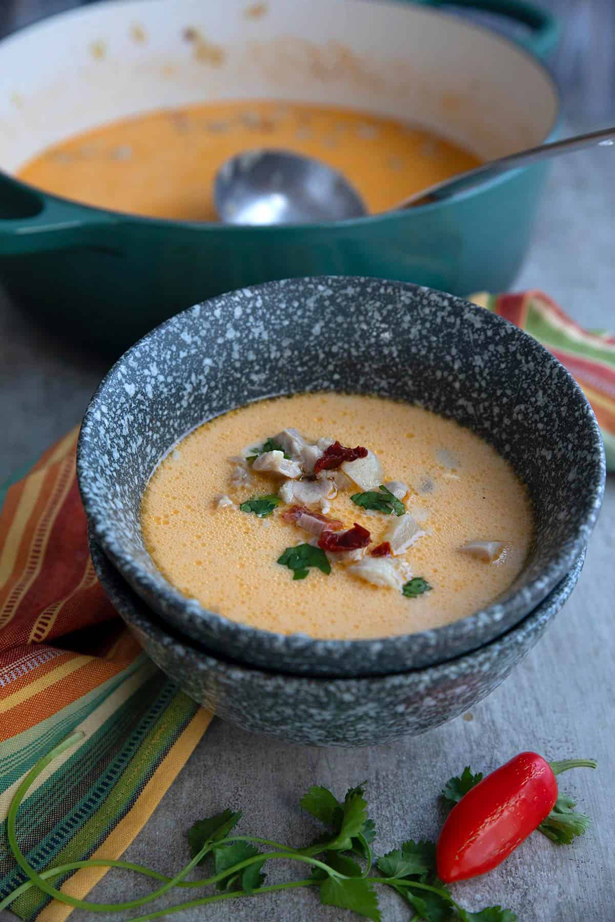 Two gray bowls stacked up with the top one filled with Chipotle Chicken Chowder, with bacon and cilantro sprinkled on top.