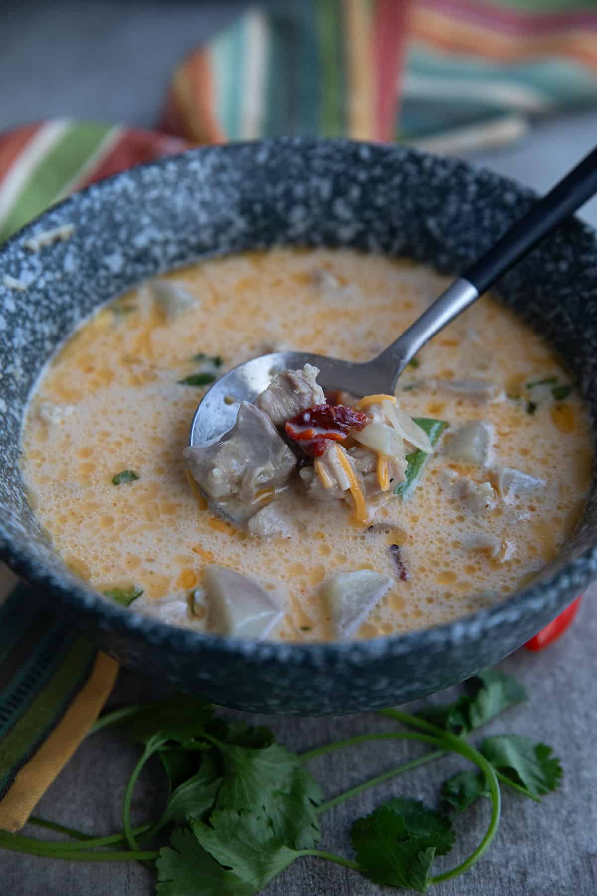 Close up shot of Keto Chipotle Chicken Chowder in a rustic gray bowl with a spoon digging into it.