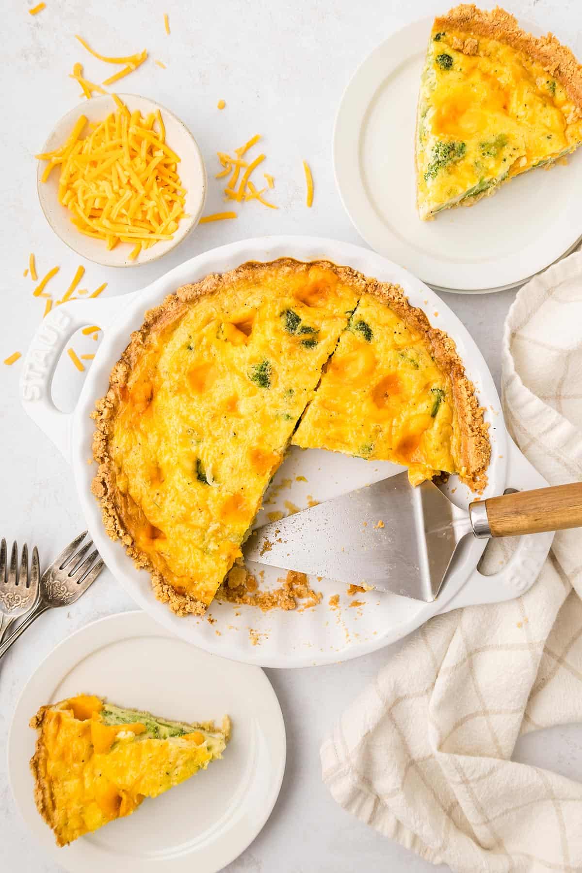 Top down image of Keto Broccoli Cheese Quiche in a white pie plate with two slices on white plates.