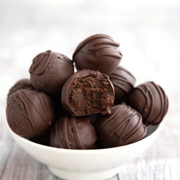 Keto Brownie Batter Truffles piled in a white bowl on a gray wooden table with a bite taken out of one.