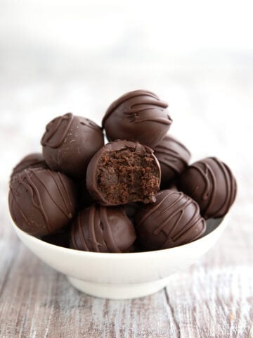 Keto Brownie Batter Truffles piled in a white bowl on a gray wooden table with a bite taken out of one.