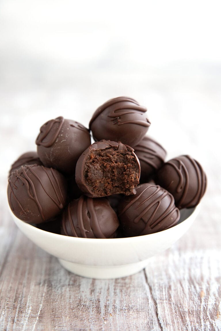 Keto Brownie Batter Truffles piled in a white bowl on a gray wooden table with a bite taken out of one.