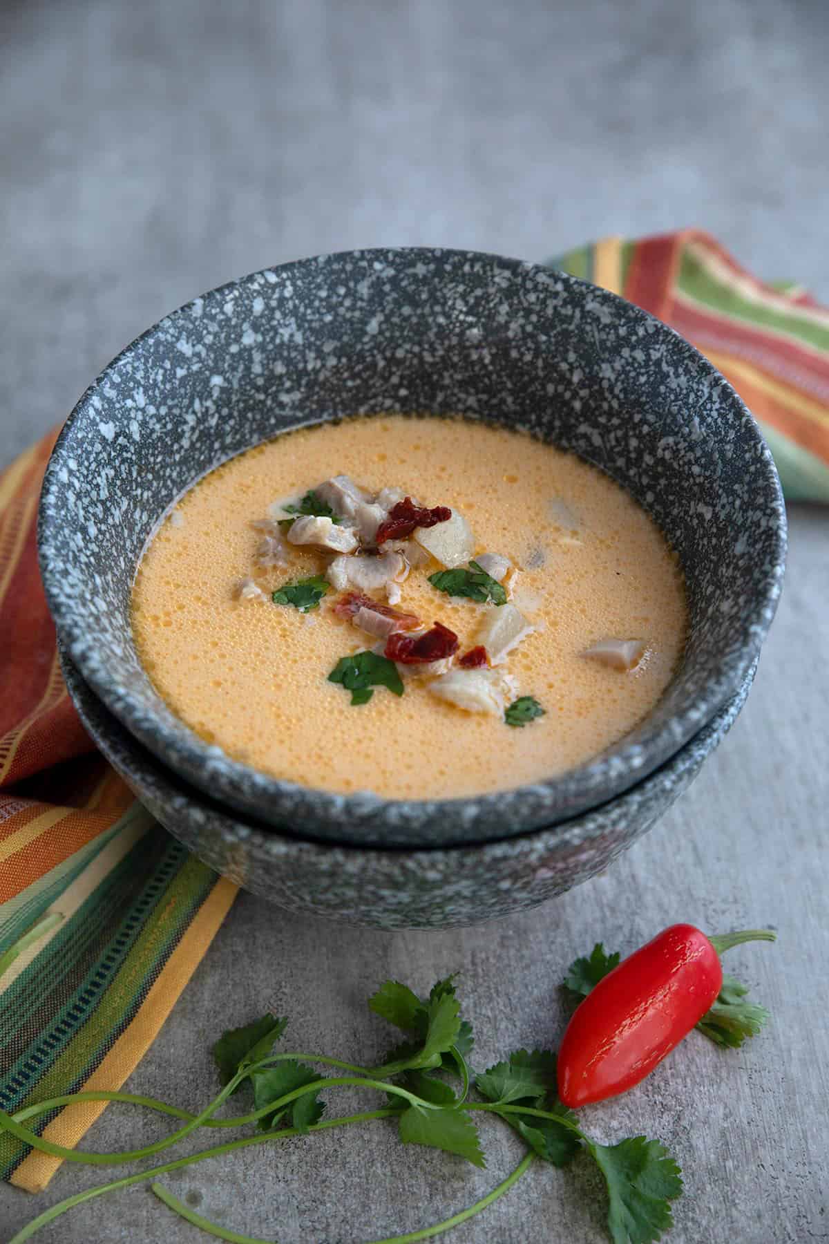 Two gray speckled bowls stacked on each other, with the top one filled with Keto Chipotle Chicken Chowder.