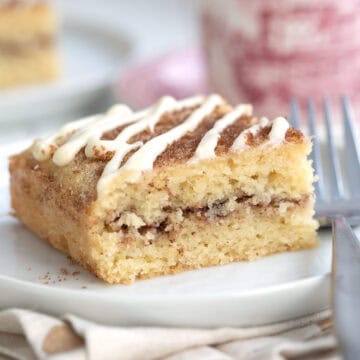 Close up shot of a slice of Keto Cinnamon Roll Coffee Cake on a white plate with a patterned red coffee cup in the background.