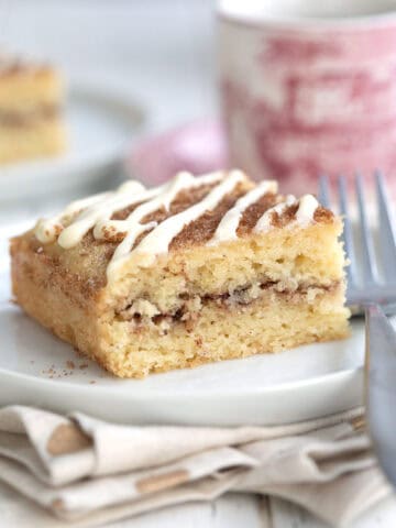 Close up shot of a slice of Keto Cinnamon Roll Coffee Cake on a white plate with a patterned red coffee cup in the background.