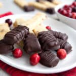 Keto Cranberry Orange Shortbread with ends dipped in chocolate piled up on a white plate over a red plaid napkin.