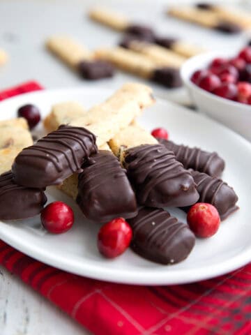 Keto Cranberry Orange Shortbread with ends dipped in chocolate piled up on a white plate over a red plaid napkin.