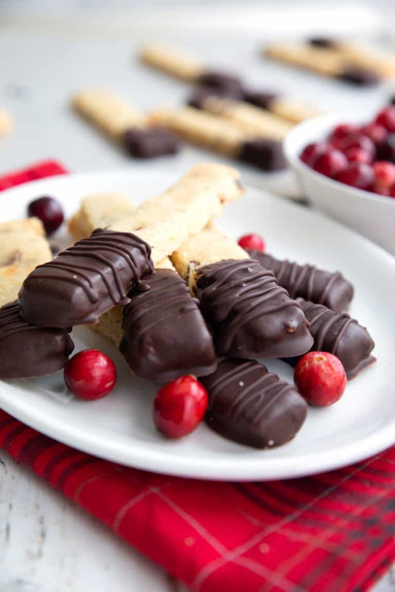 Keto Cranberry Orange Shortbread with ends dipped in chocolate piled up on a white plate over a red plaid napkin.