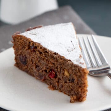 Close up shot of a slice of Keto Holiday Fruitcake on a white plate with a fork.