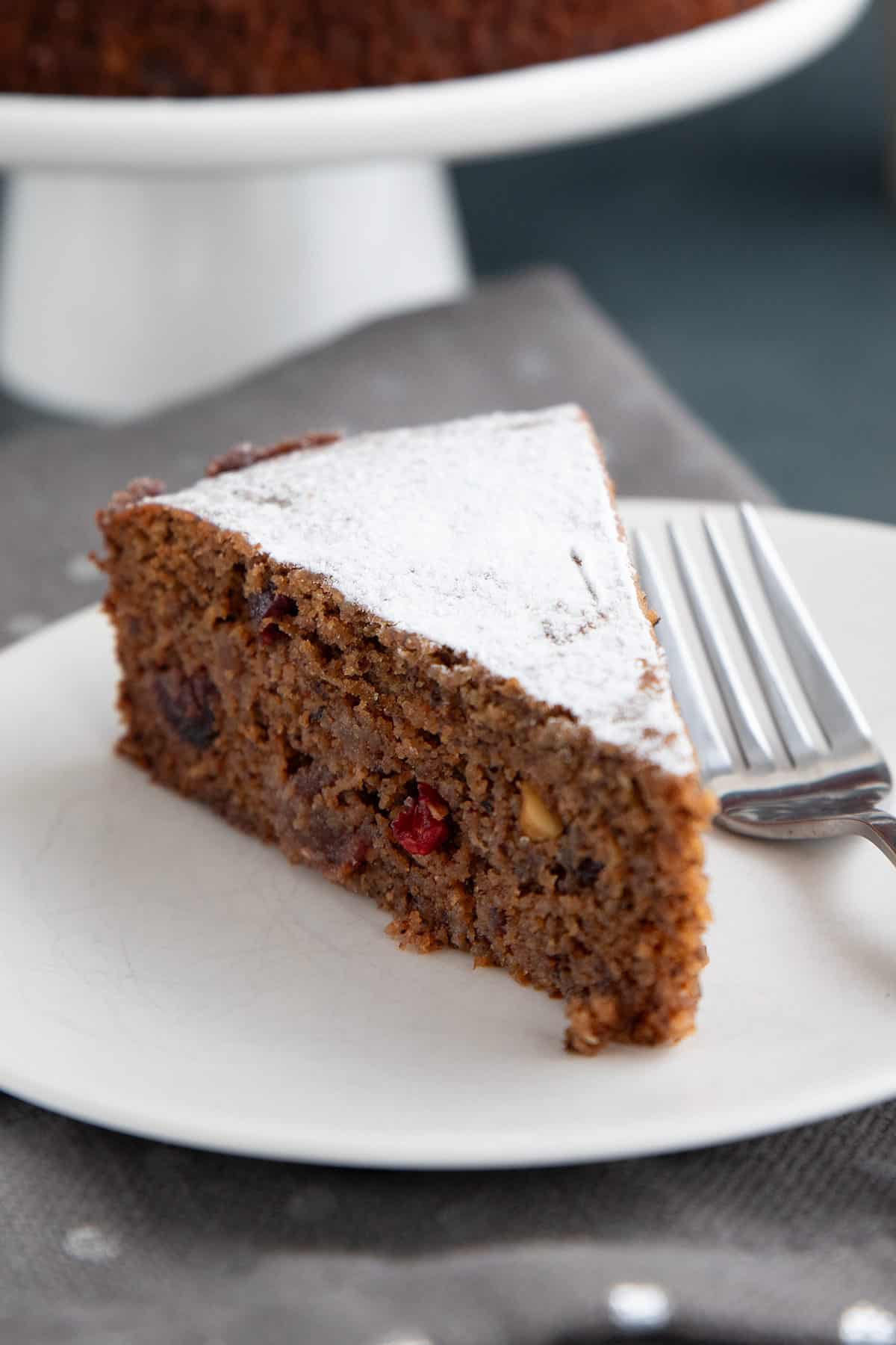 Close up shot of a slice of Keto Holiday Fruitcake on a white plate with a fork.