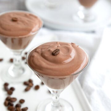 Glass dishes filled with protein mousse on a white platter, with coffee beans strewn around.