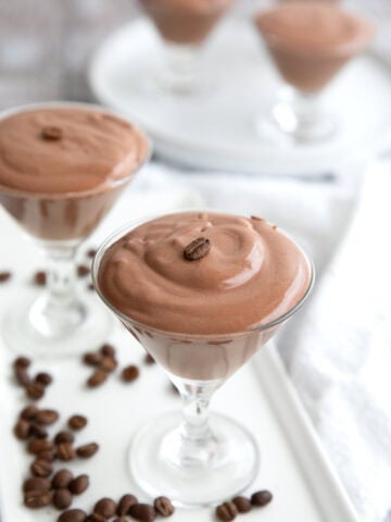 Glass dishes filled with protein mousse on a white platter, with coffee beans strewn around.