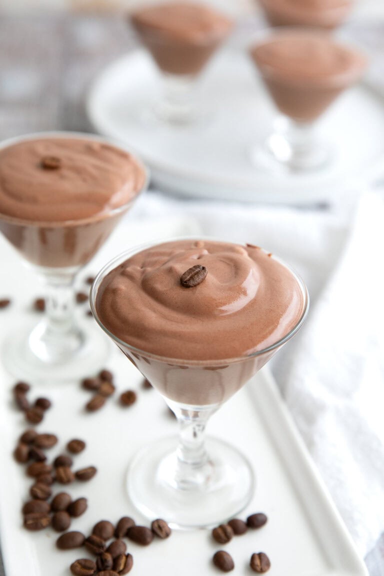 Glass dishes filled with protein mousse on a white platter, with coffee beans strewn around.