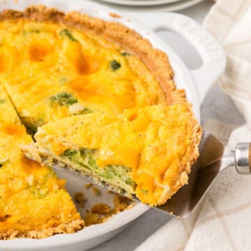 A slice of Keto Broccoli Cheese Quiche being lifted out of a white pie plate.