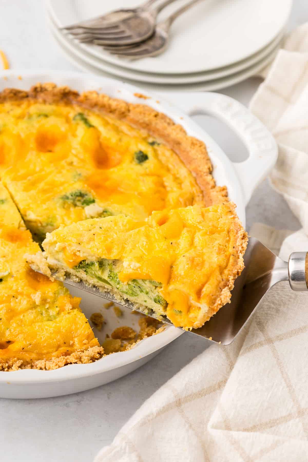 A slice of Keto Broccoli Cheese Quiche being lifted out of a white pie plate.