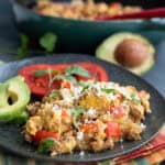 Chorizo and eggs on a black plate with avocado and tomatoes, over a striped napkin.