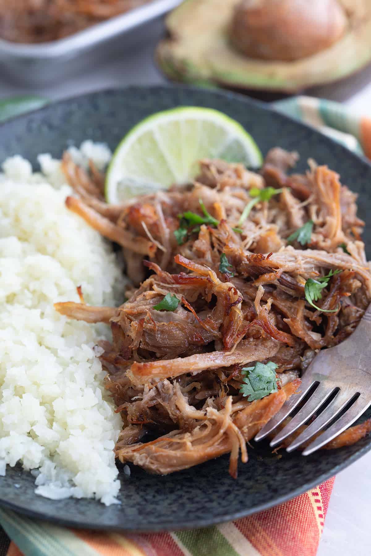 Keto Pork Carnitas close up on a black plate with cauliflower rice and a slice of lime.