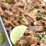 Titled Pinterest image of keto carnitas on a baking sheet with chopped cilantro and slices of lime.