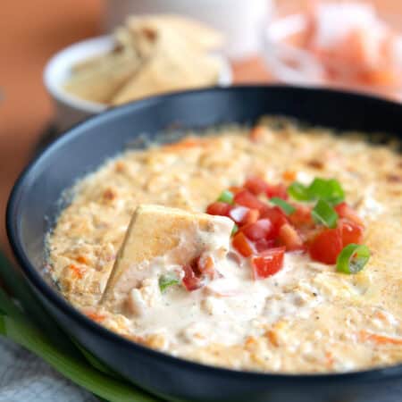 A keto cracker digging into a bowl of Baked Shrimp Dip.