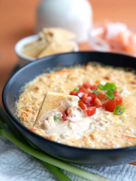 A keto cracker digging into a bowl of Baked Shrimp Dip.