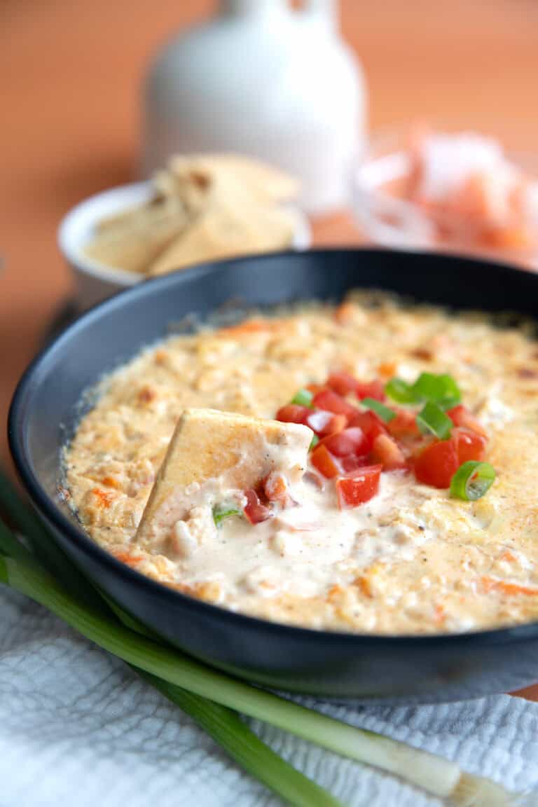 A keto cracker digging into a bowl of Baked Shrimp Dip.