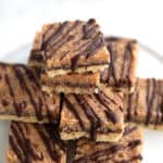 Keto Samoa Cookie Bars piled up on a white cake stand on a white table.