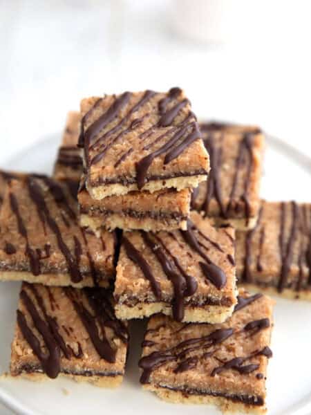 Keto Samoa Cookie Bars piled up on a white cake stand on a white table.